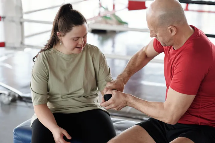 A boxing coach wrapping the hands of a young woman with Down syndrome before a session