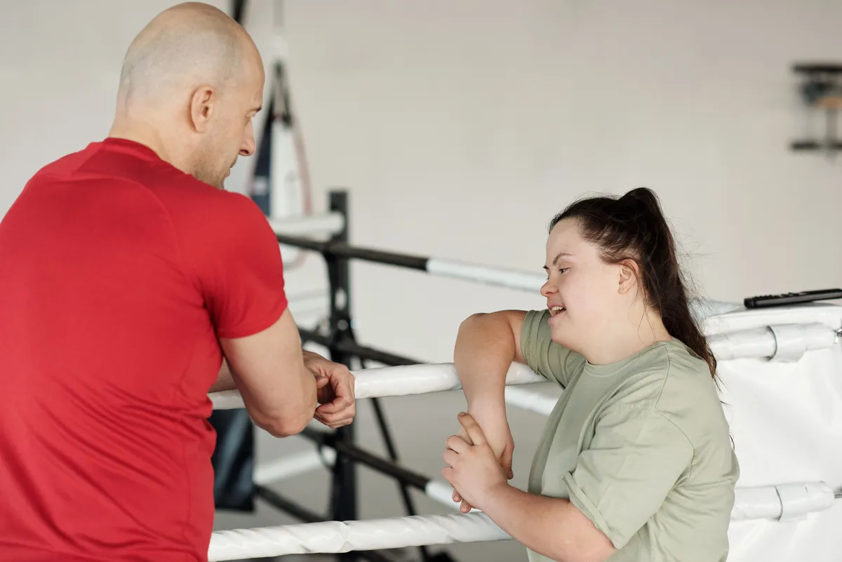 A boxing coach and a young woman with Down syndrome talking together at a community gym