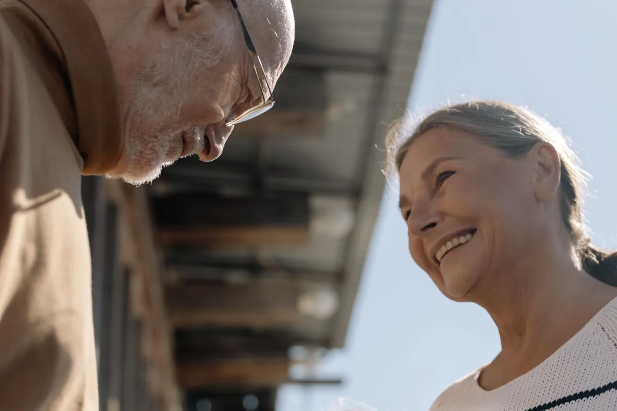 A senior man and a caregiver smiling at each other outdoors