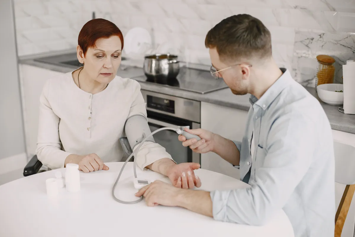 A caregiver taking a senior woman's blood pressure in her kitchen