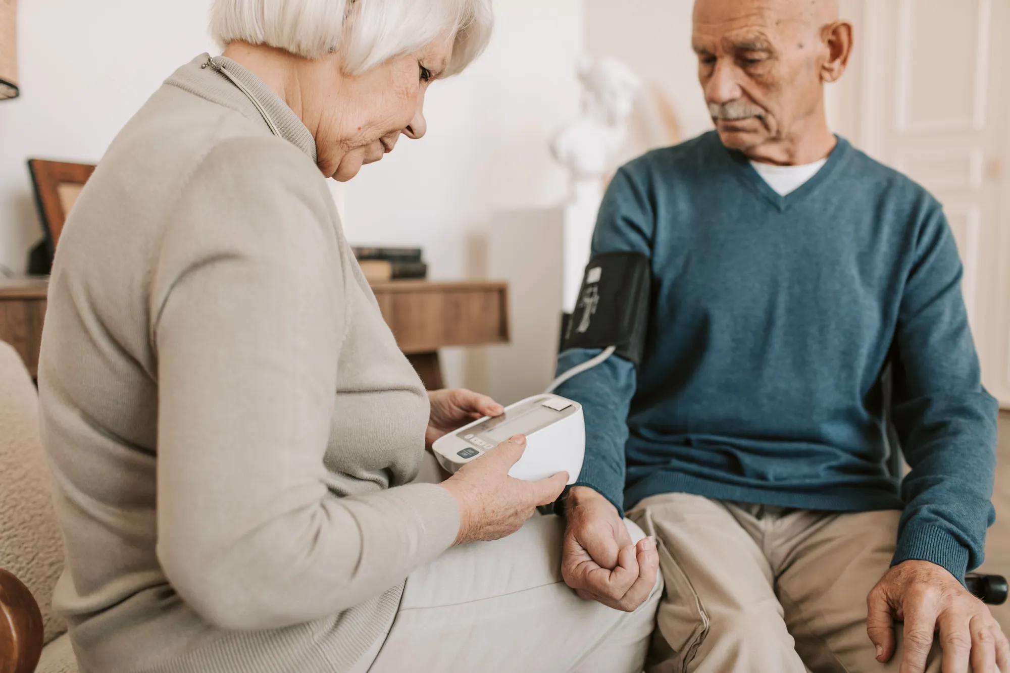 A caregiver checking a senior man's blood pressure at home and recording the reading