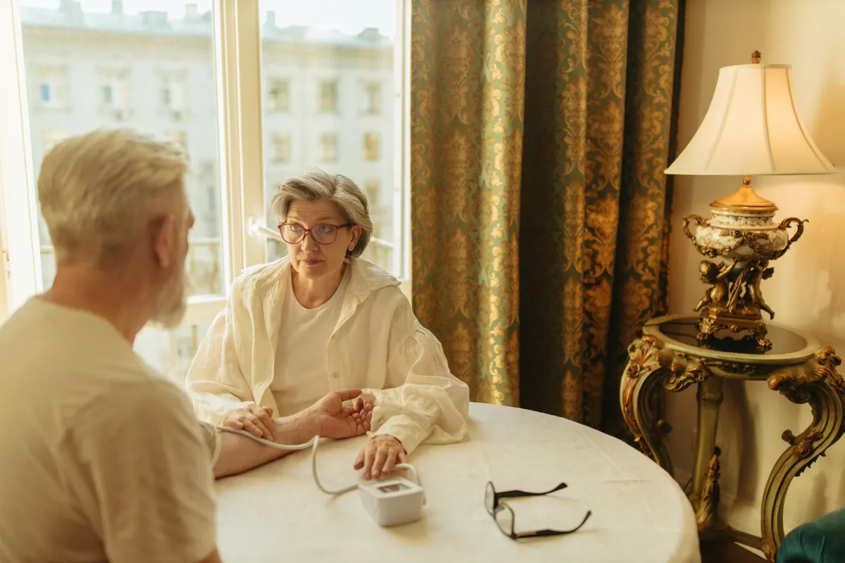 A caregiver checking a senior man's blood pressure at his kitchen table at home