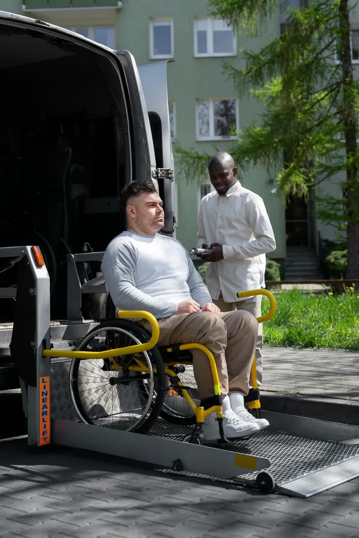 A man using a wheelchair boarding an accessible van on a lift while a worker assists