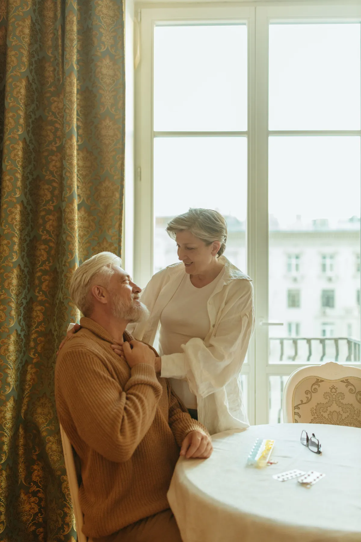 Senior woman resting her hands on her partner's shoulder as they smile at each other