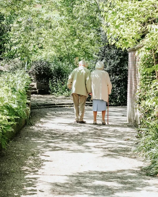 An older couple walking together down a sunlit garden path